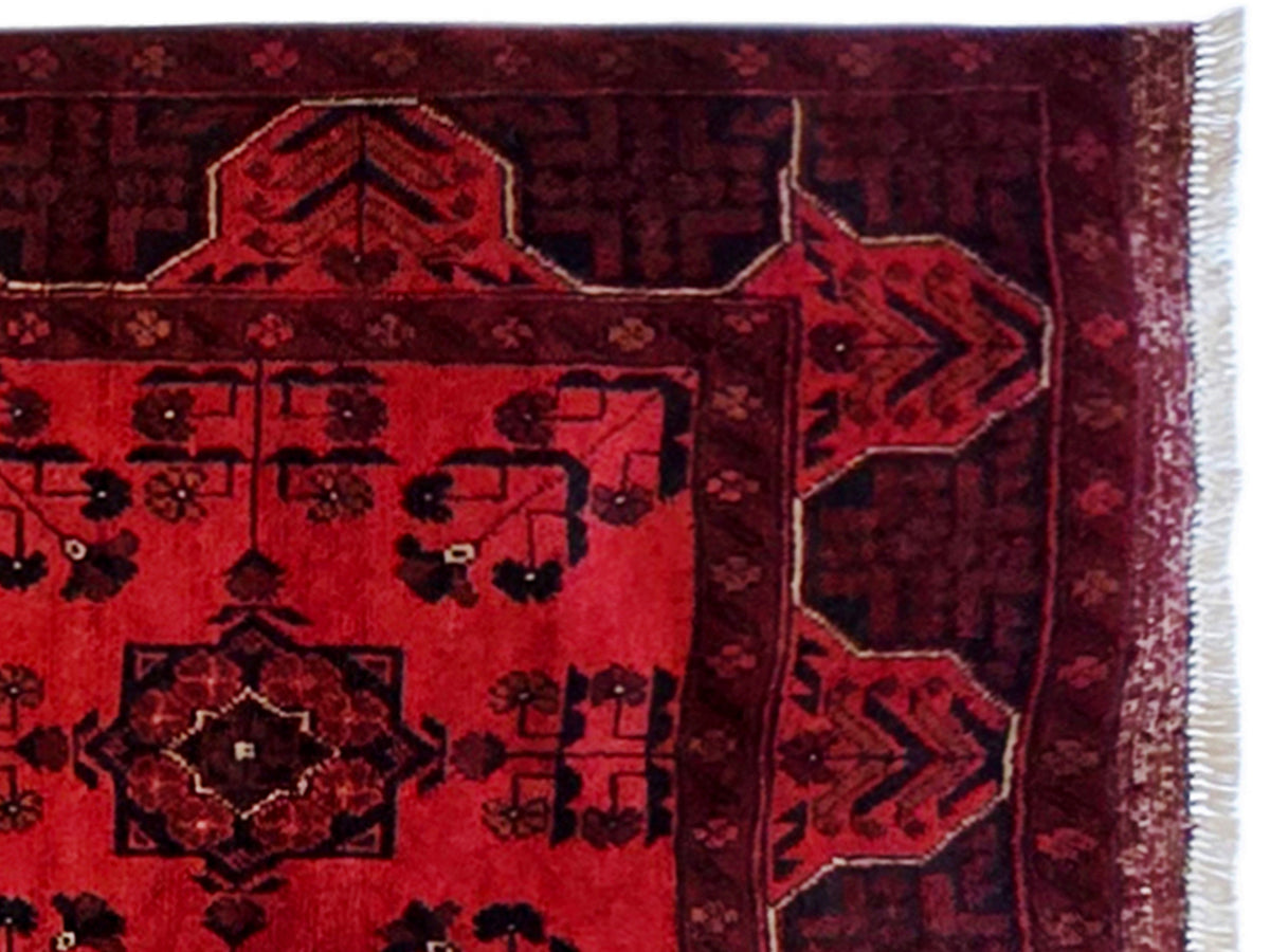 Close-up of red patterned rug with dark geometric blocks and border trim