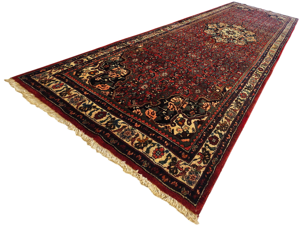 Bidjar rug angled view, red center with cream and gold geometric border, fringed ends