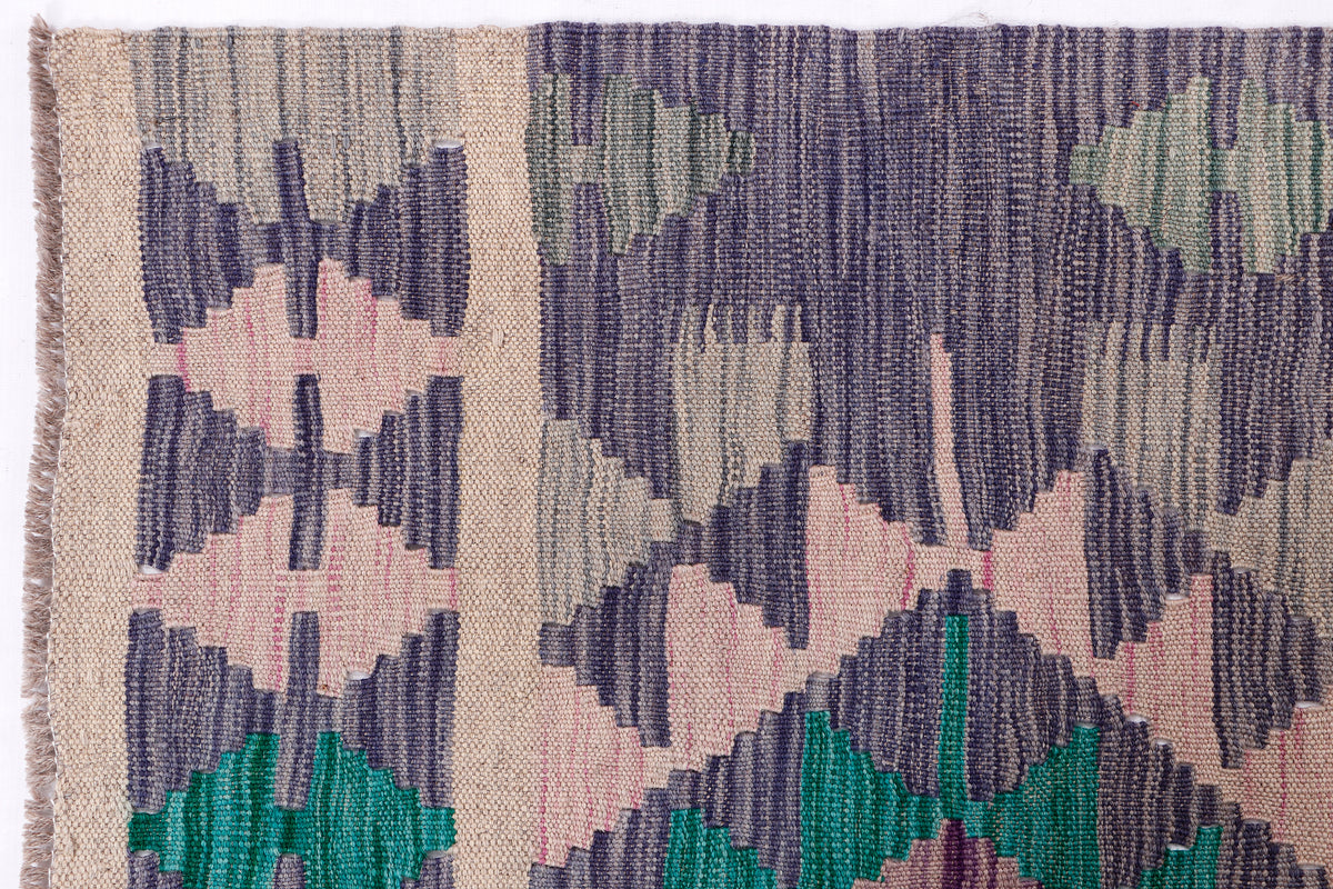 Kilim rug close-up of woven texture with grey, teal, and pink geometric shapes