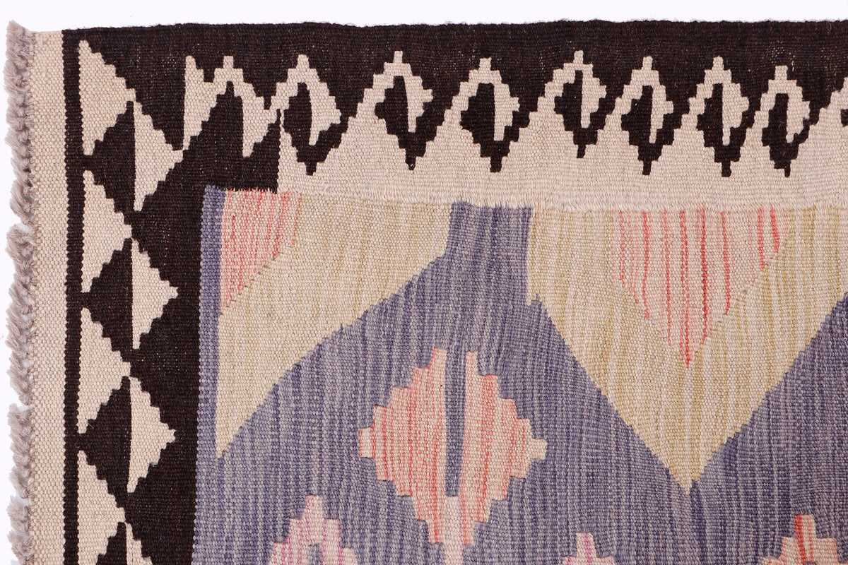 Kilim rug corner with black zigzag border and pastel purple, peach, and cream motifs.