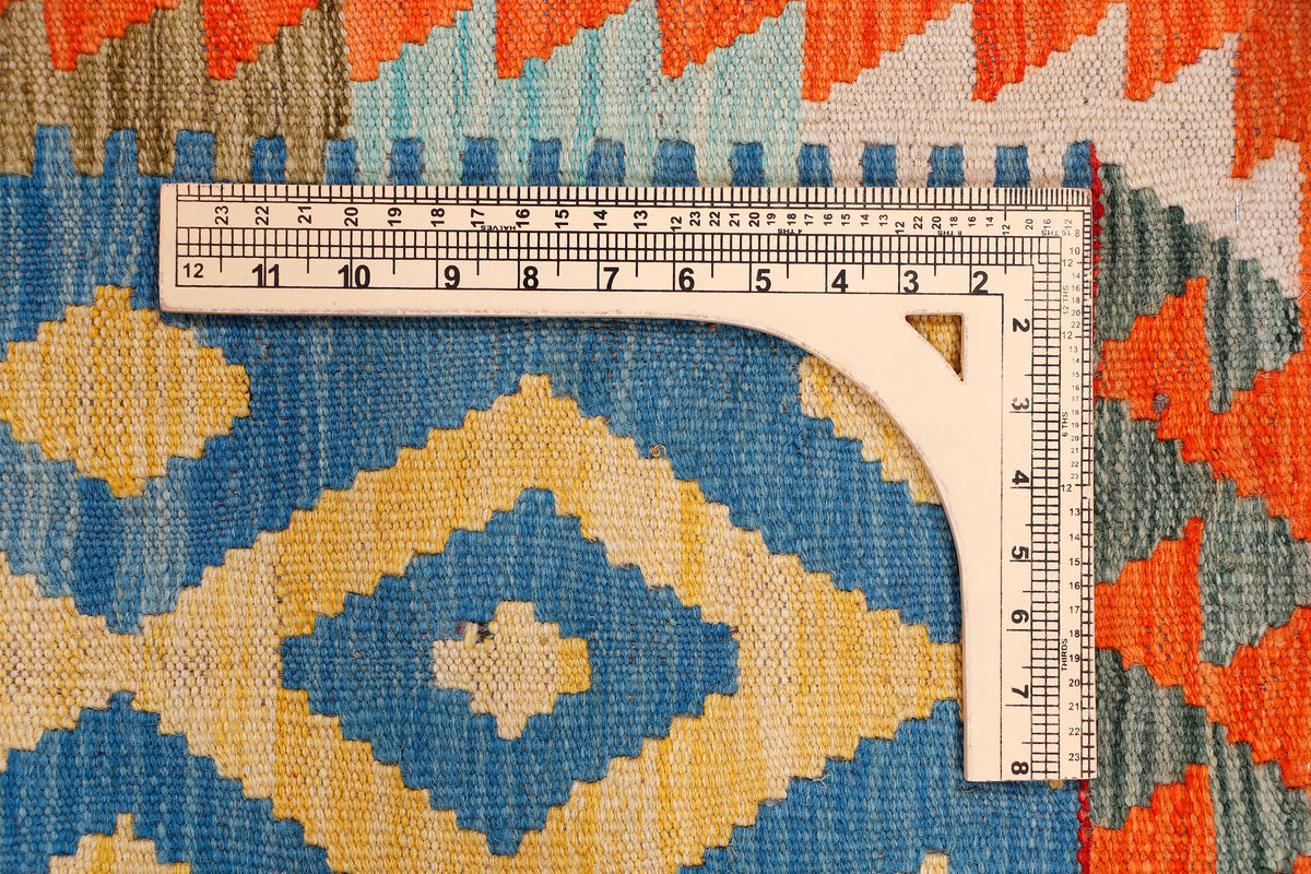 Kilim rug fabric close-up with ruler, featuring blue and beige diamond motif and orange accents