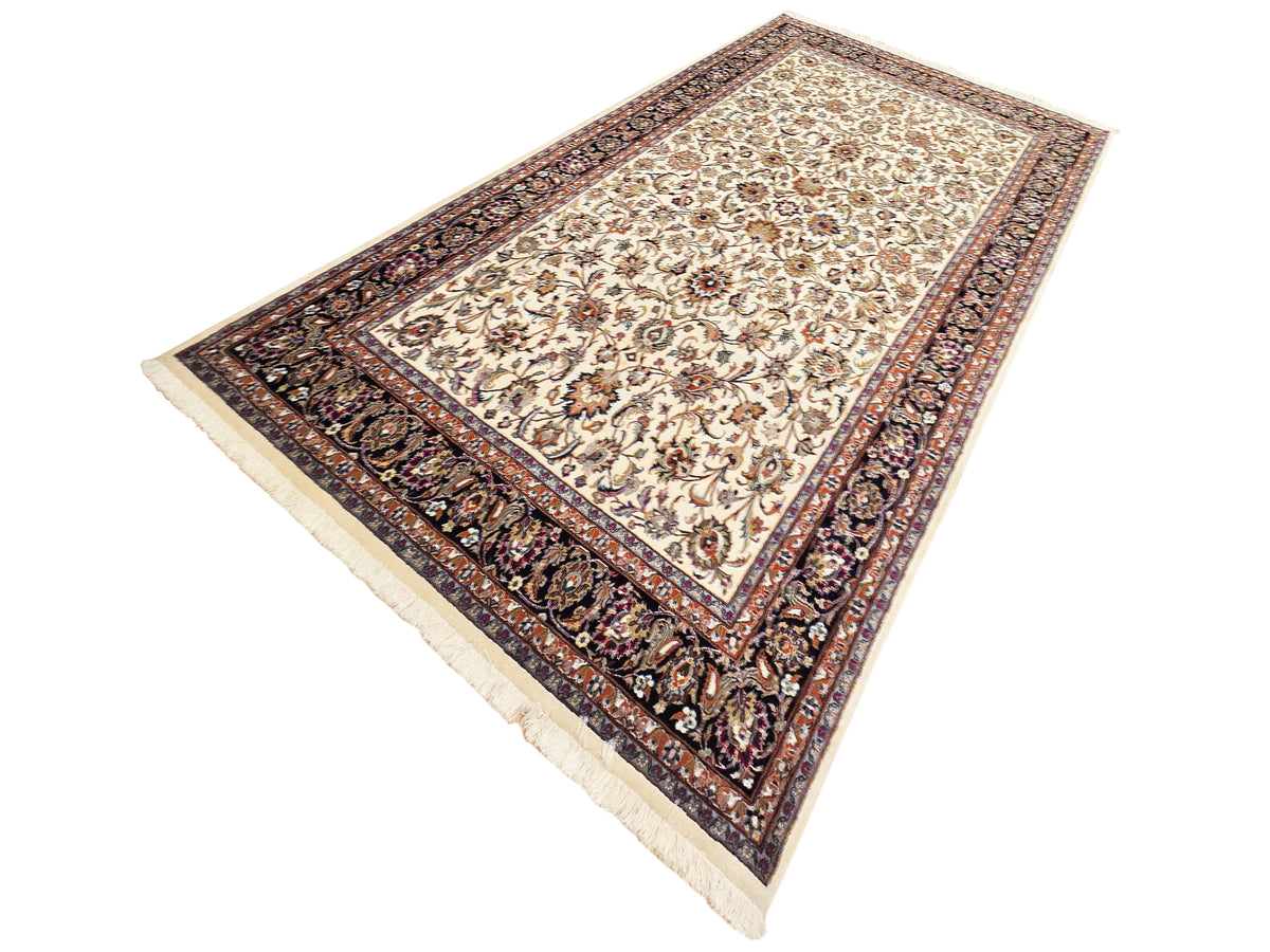 Folded view of cream floral rug with dark navy decorative border and fringes