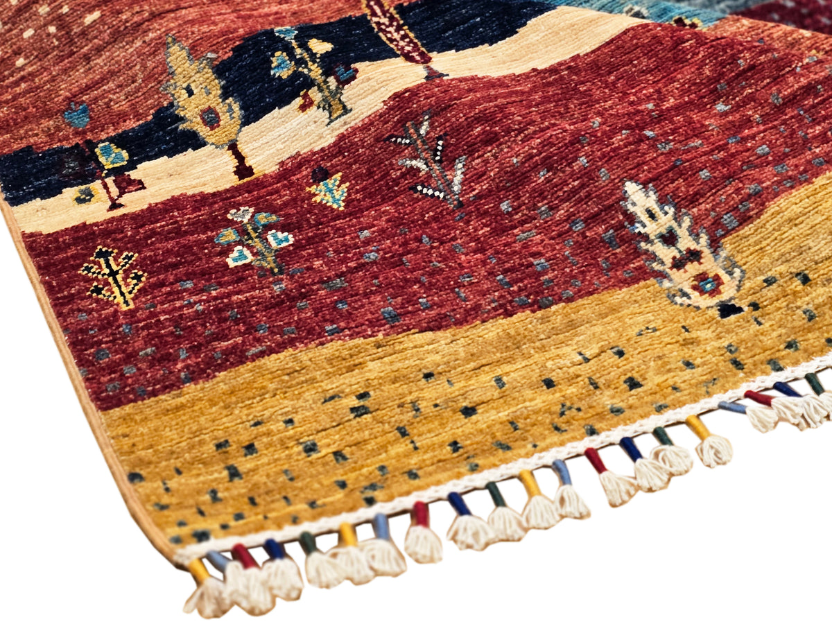 Ariana Gabbeh rug corner with red field, teal accents, tan stripe, and fringe trim.