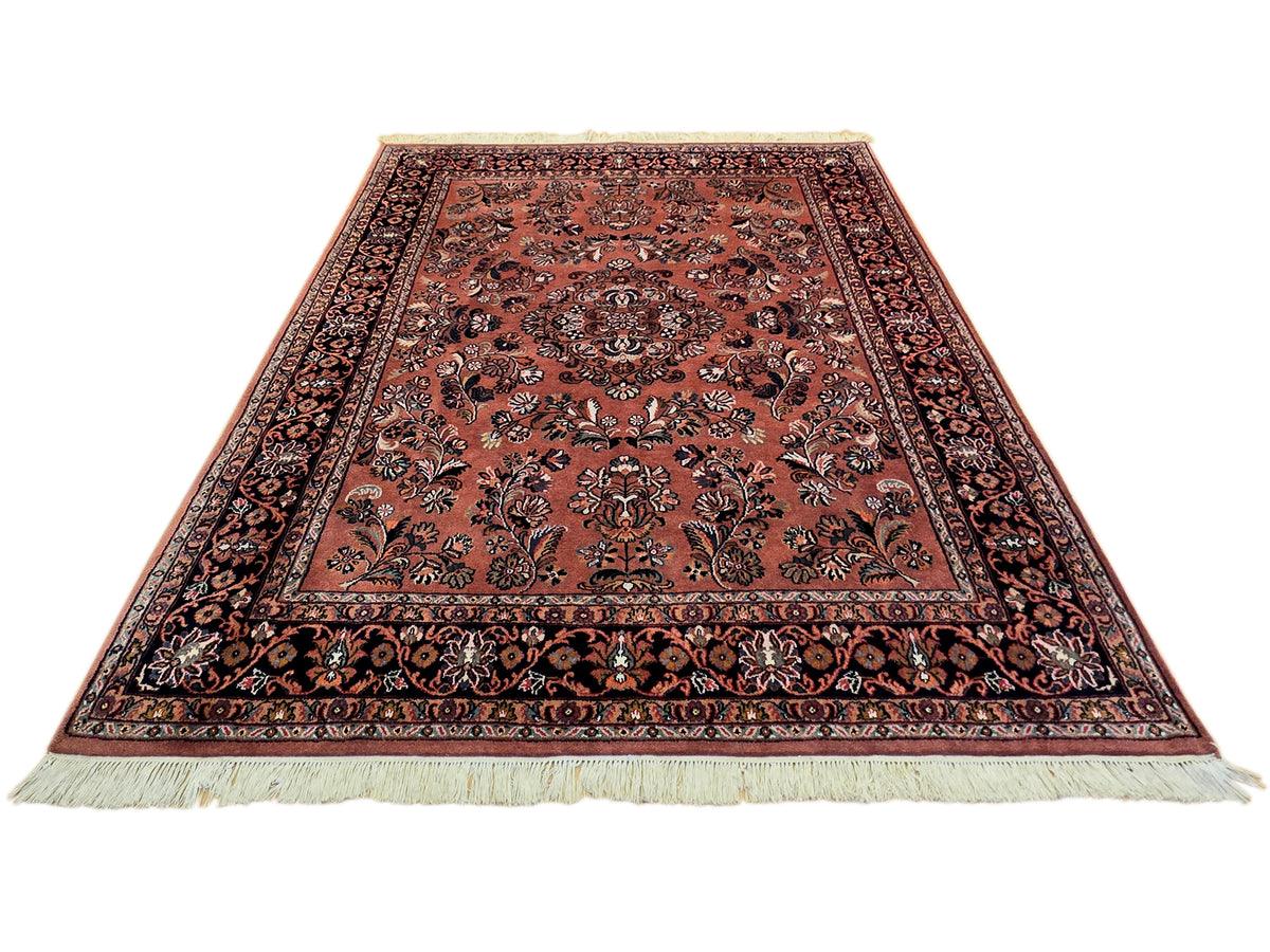 Terracotta rug with central floral motif and dark border, short fringe along edges