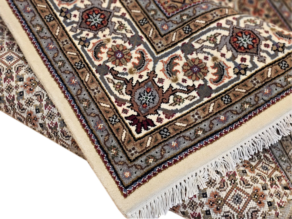 Ornate patterned area rug with cream border, dark blue accents, and fringed edge.