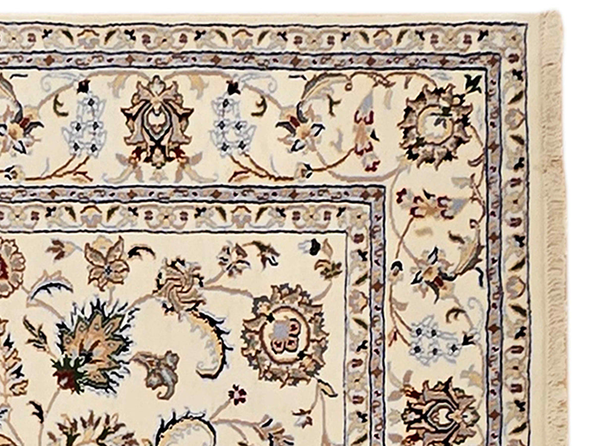 Close-up section of cream rug with decorative floral rosettes, thin blue outline, fringed edge