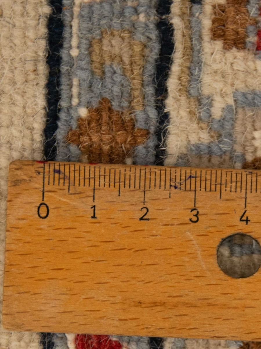 Rug pile close-up with beige, navy, and brown woven pattern; ruler for scale