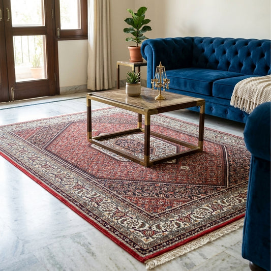 Red ornamental area rug on a floor with detailed border and cream fringe in a room