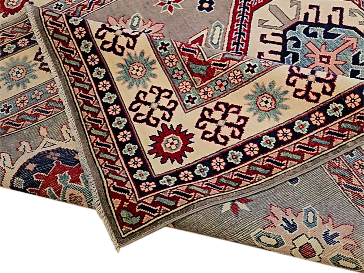 Kazak rug close-up corner with red, navy, and cream geometric motifs and braided trim