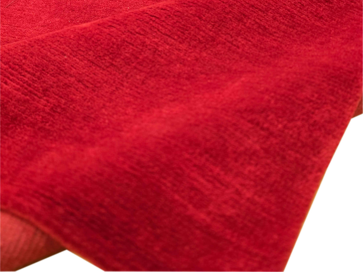 Red rug corner close-up with short, textured pile and smooth binding edge