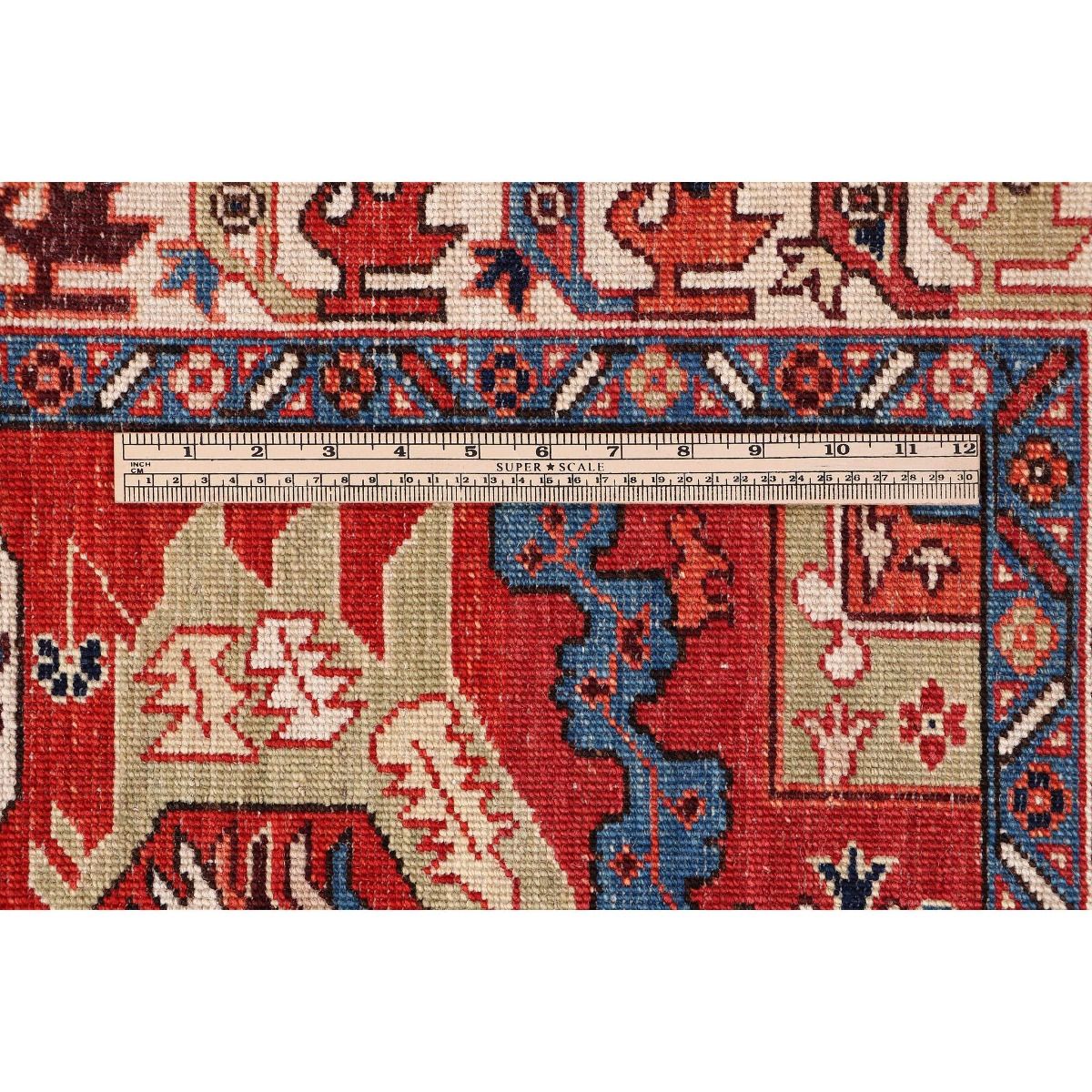 Red Kazak rug close-up with measuring tape along edge; cream and navy pattern