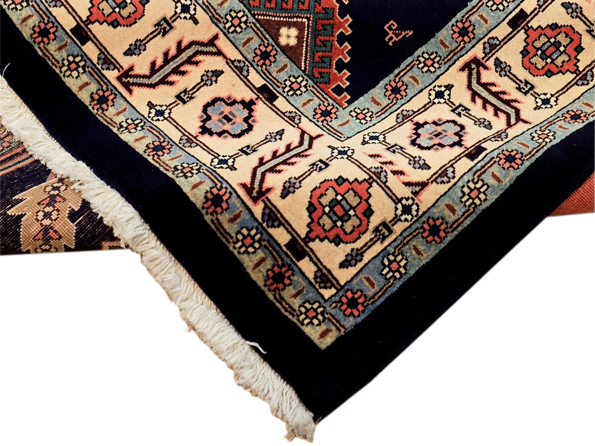 Ornate navy rug corner with cream border, red motifs, and light fringe edge