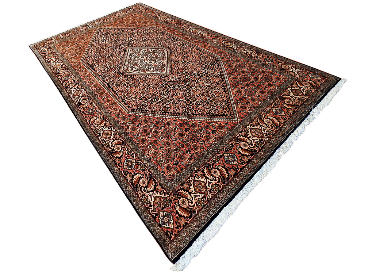 Rust, black and cream area rug with medallion design and decorative border, light fringe edge.