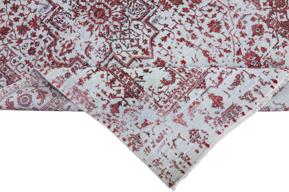 Corner detail of light gray rug with distressed red floral and geometric motifs