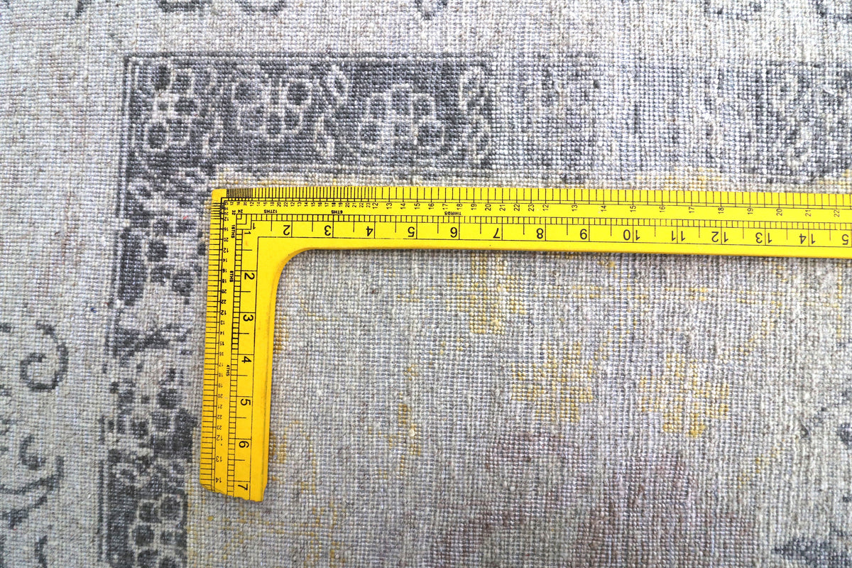 Light gray rug corner detail with blue and yellow motifs and measuring tape for size.
