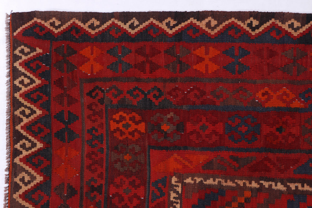 Red kilim rug close-up with blue and brown geometric bands and fringe edge.