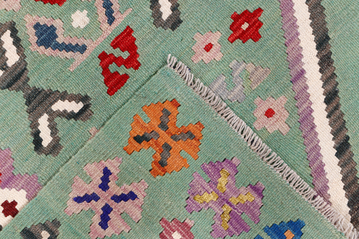Green kilim rug with multicolor cross motifs and fringed border