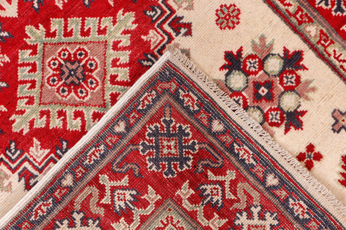 Kazak rug corner close-up, red field with cream medallions and decorative border