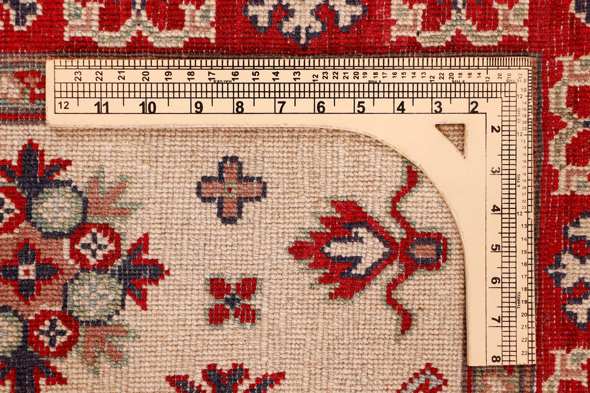 Kazak red rug close-up with cream field, geometric motifs and ruler measuring length