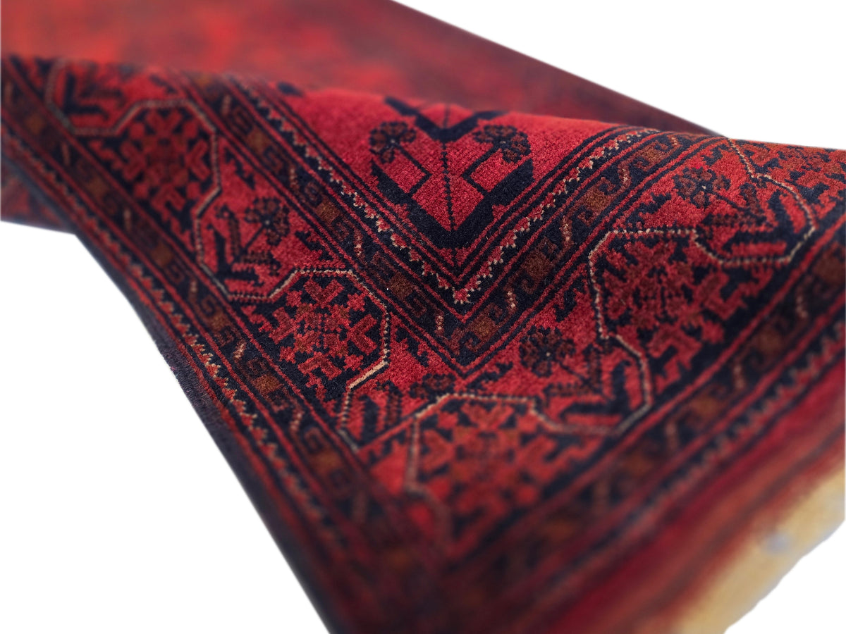 Close-up of Khanmohamad rug corner with deep red field, dark motifs, and woven texture.