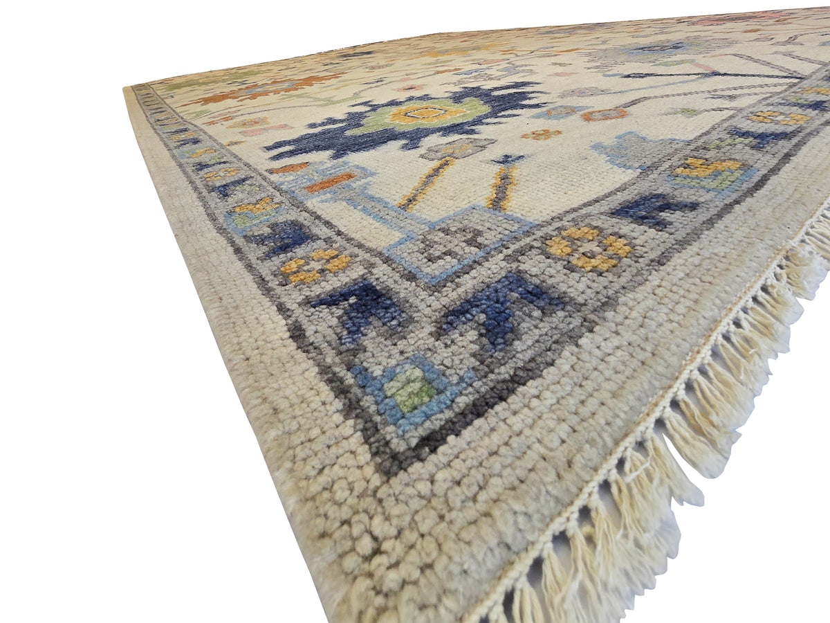 Oushak rug with short fringe, ivory base, navy diamond center, and blue and gold accents