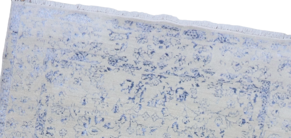 Top border of ice blue rug with distressed floral print and short fringes