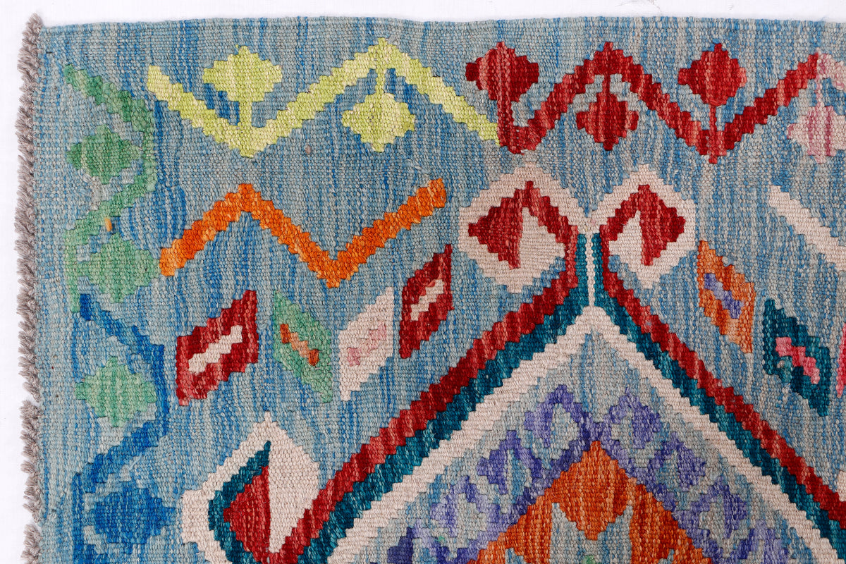 Close-up of blue kilim rug with star and diamond pattern in green, red, purple, and orange