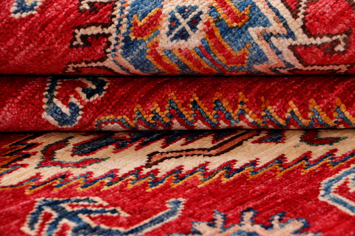 Red rug with rolled edge showing close-up geometric motifs in blue and cream