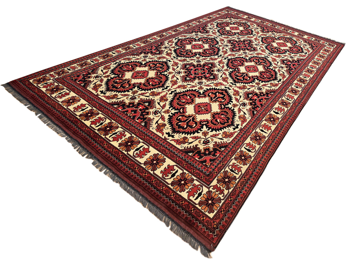 Afghan rug shown diagonally: cream and red pattern with dark border and fringed selvage corners.