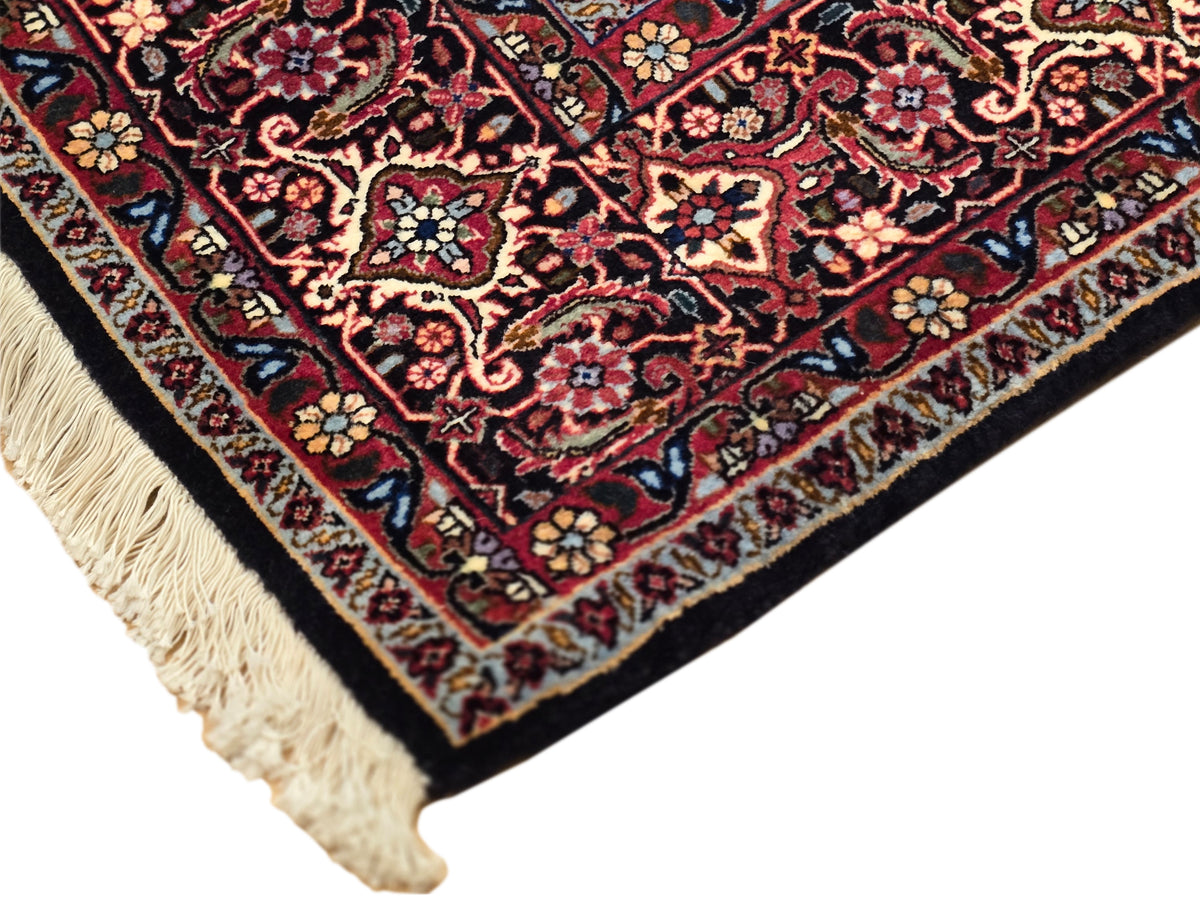 Bidjar rug corner close-up with red floral motifs, dark navy outlines, and fringe