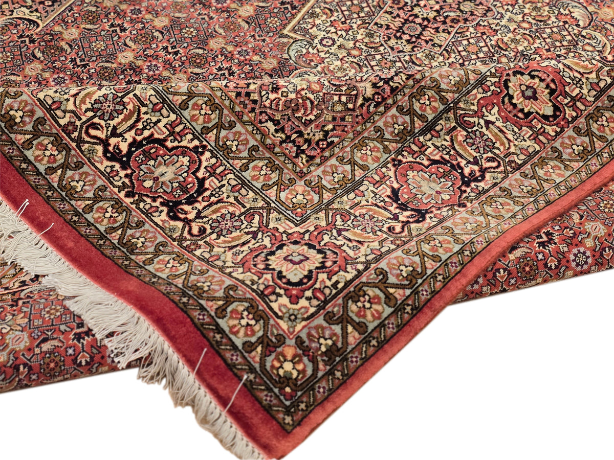 Bidjar rug corner close-up with red background, patterned border, and cream fringe trim.