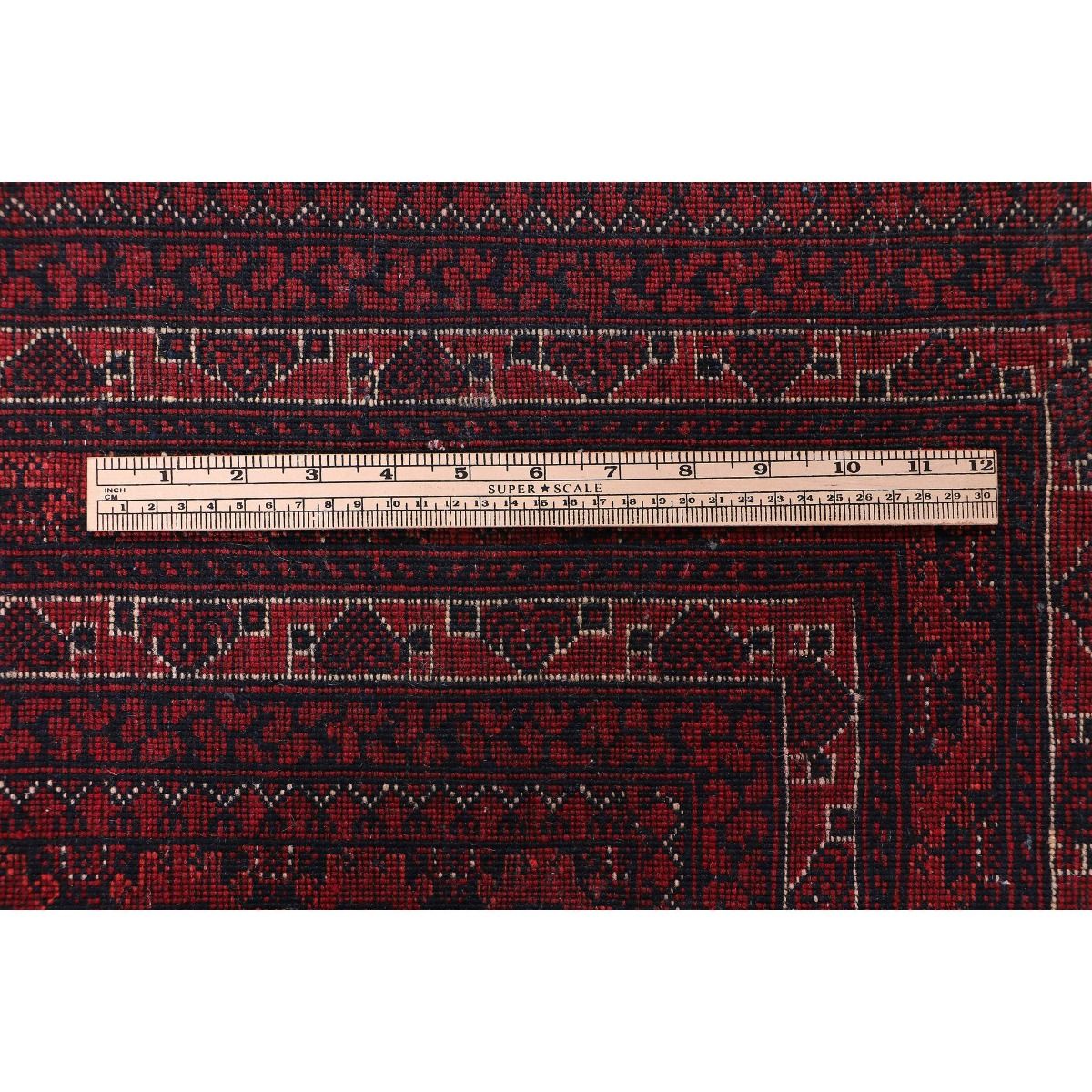 Red Bukhara rug close-up with ruler scale and fine geometric border motif