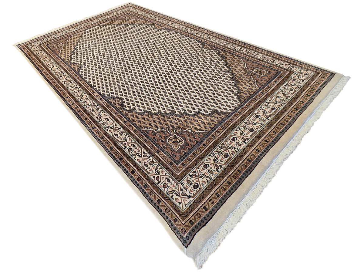 Angled view of patterned area rug with lattice medallion, dark border, and short fringe