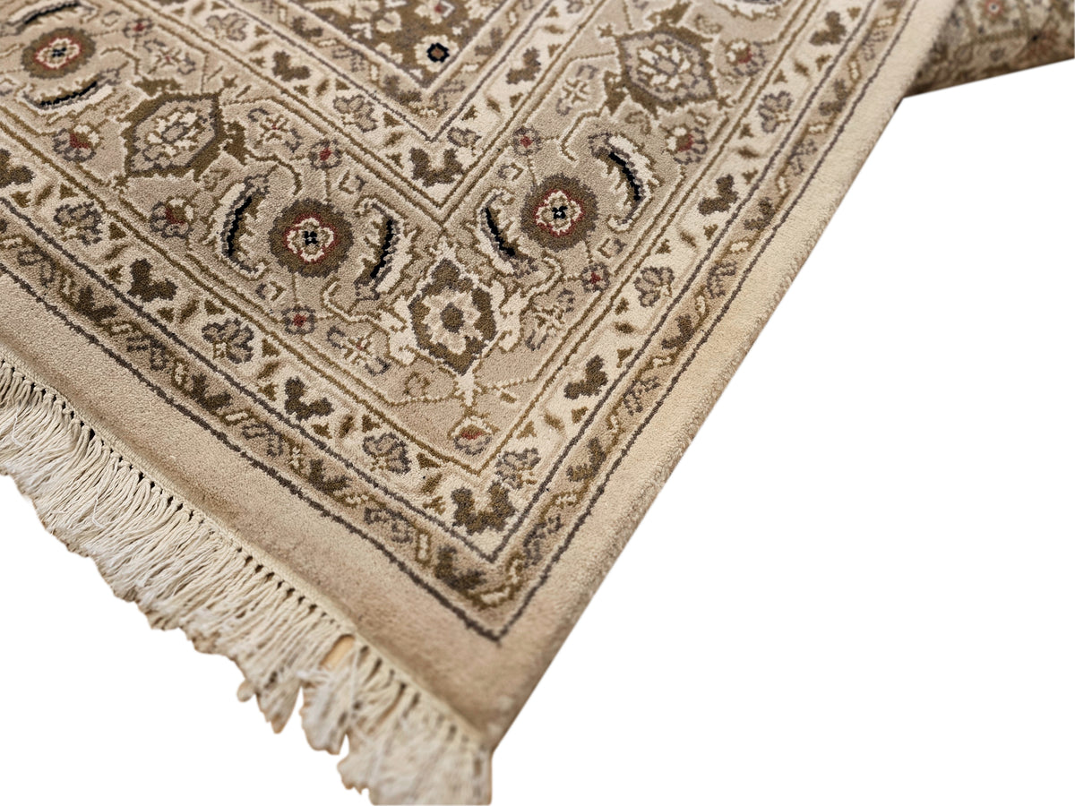 Corner detail of beige and brown patterned rug with ornate border and tassel fringe.