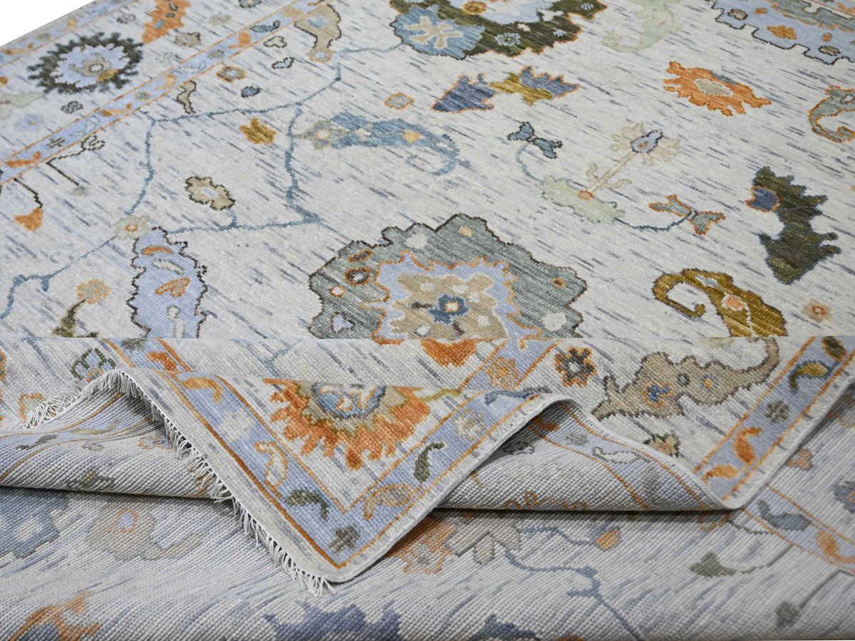 Oushak-style rug corner with fringe, light blue base and multicolor floral motifs in orange, teal