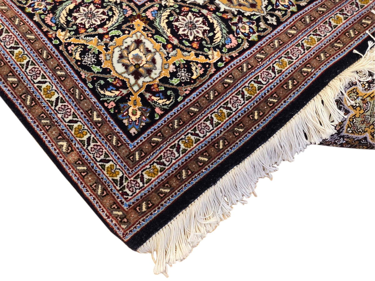 Patterned dark rug corner with cream fringe and multicolor ornamental border