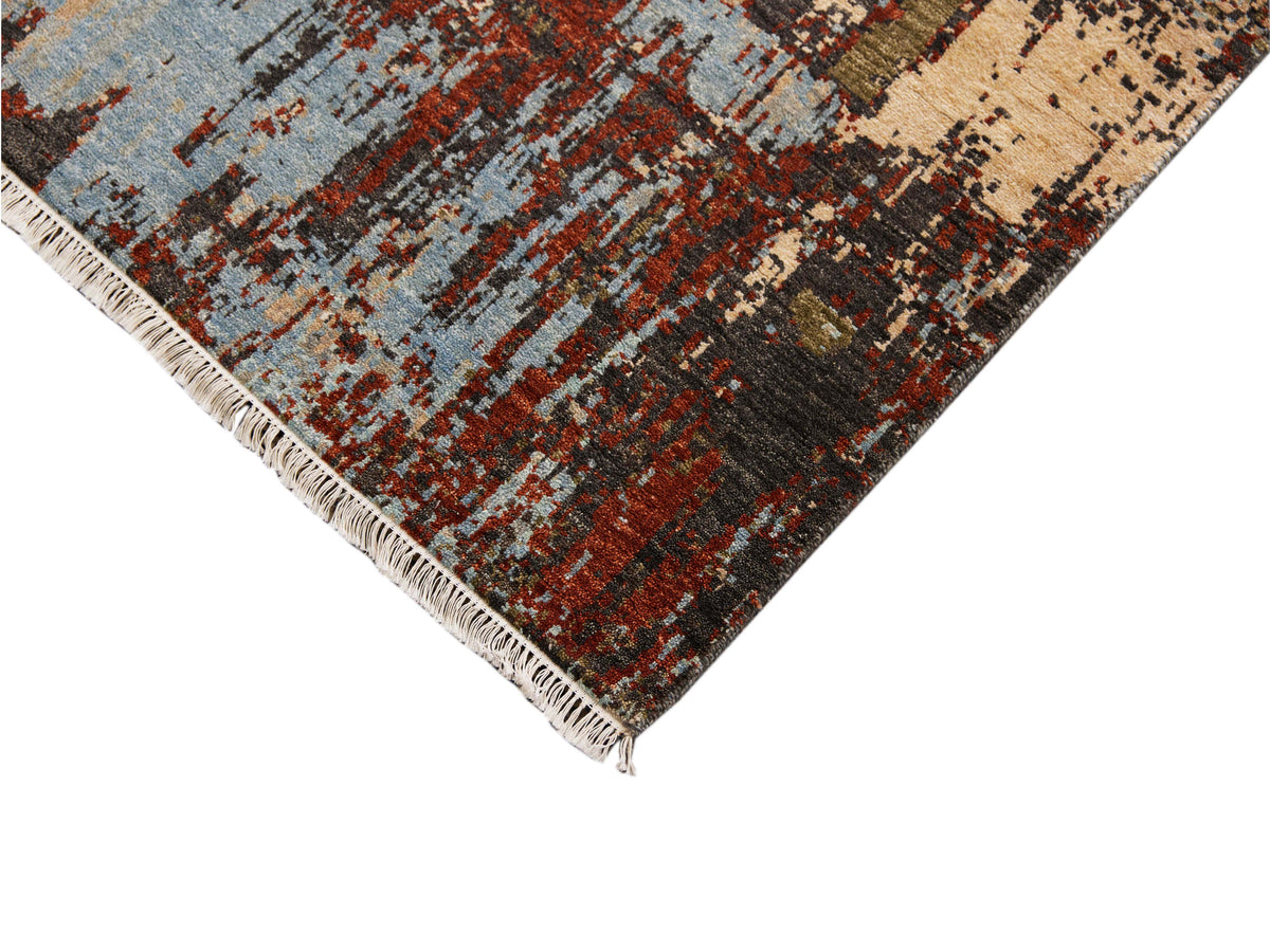 Corner view of abstract area rug with fringe trim in beige, blue and rust hues.