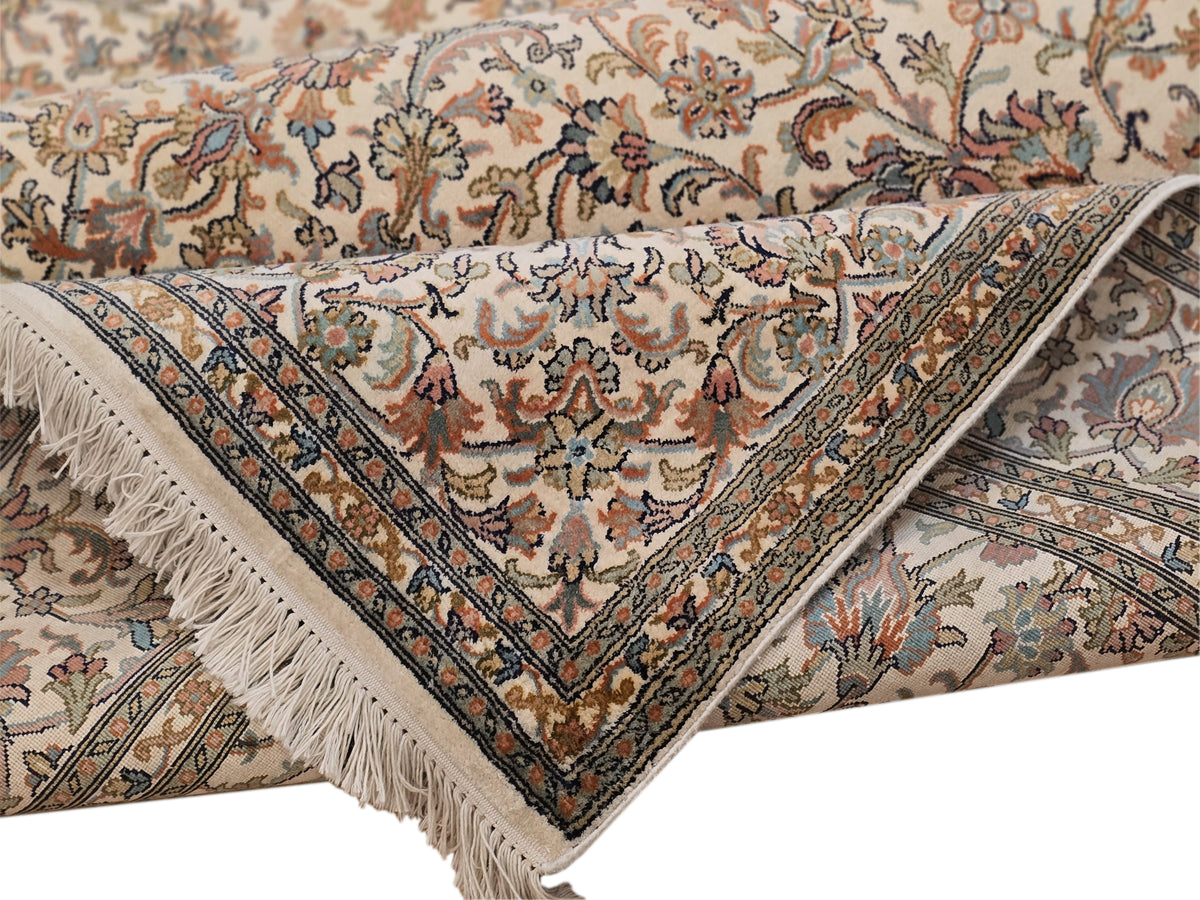 Beige silk rug fold with floral medallions, multicolor border, and long fringe