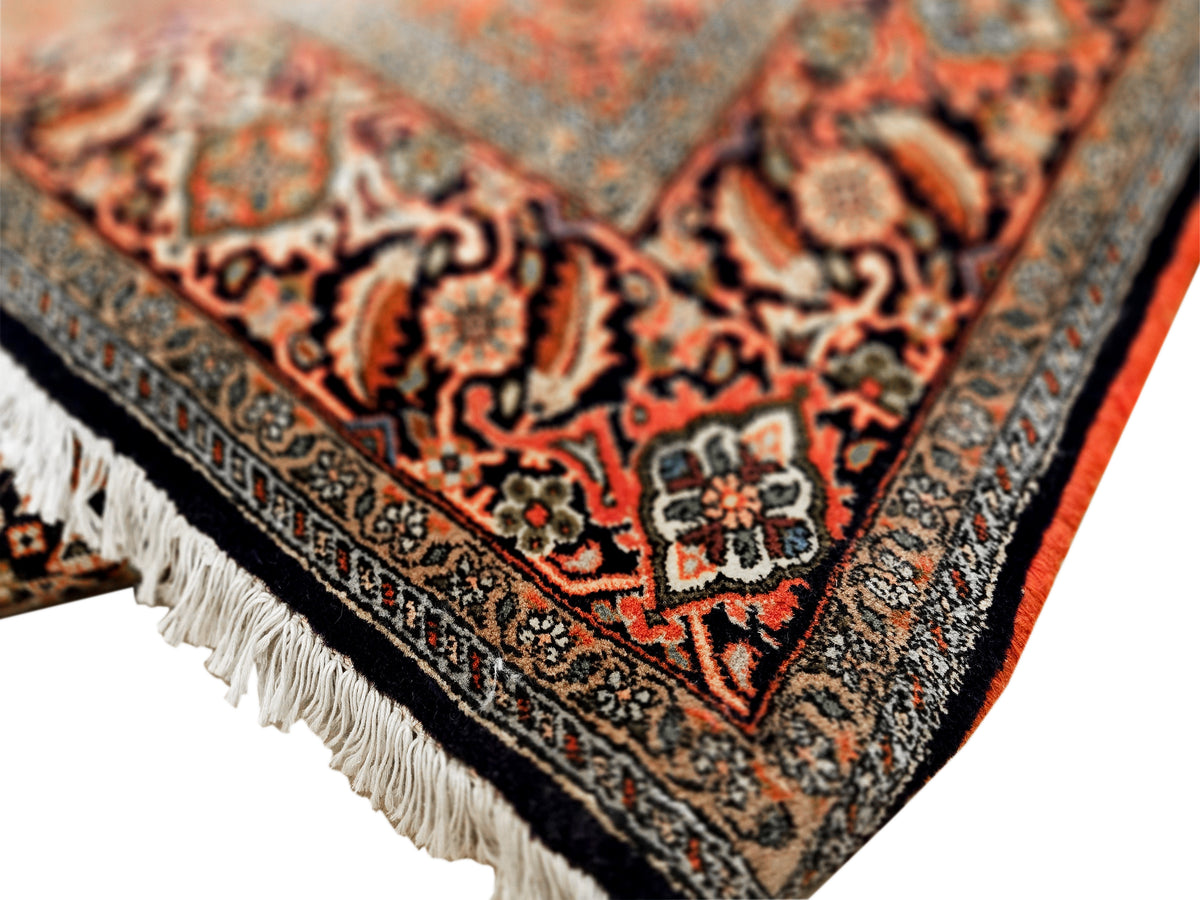 Close-up of rust, orange and black rug pattern with ornate motifs and fringe edge.