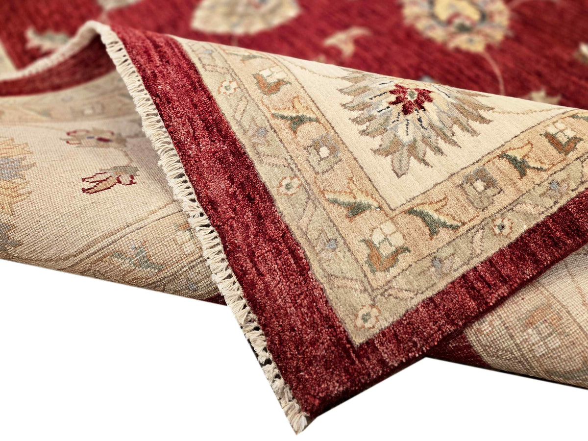 Floral area rug with burgundy border, beige field, and fringed edge, corner close-up