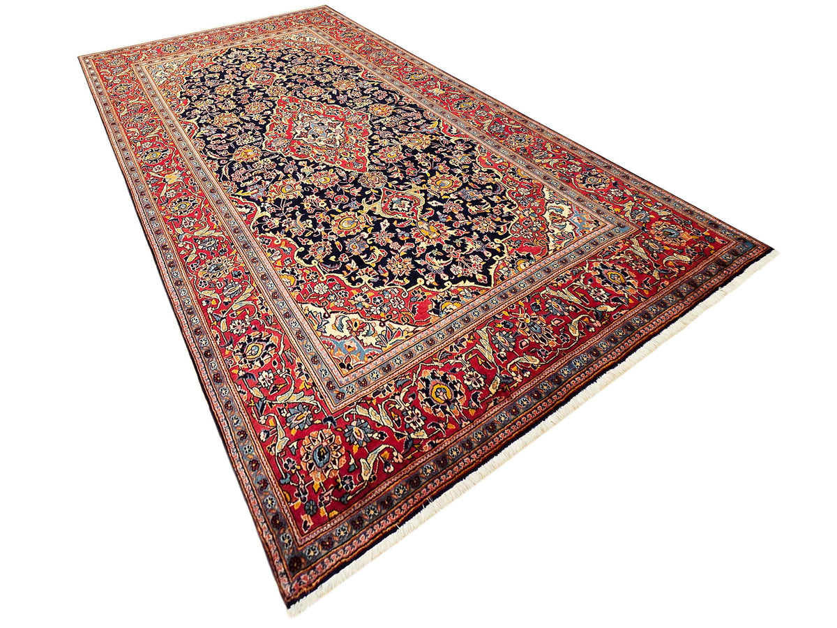 Diagonal view of red and navy Persian-style rug with ornate center medallion and border.