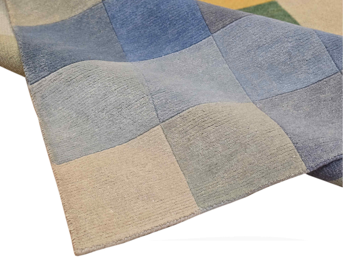 Folding corner of square-block rug in blue and gray with beige edge