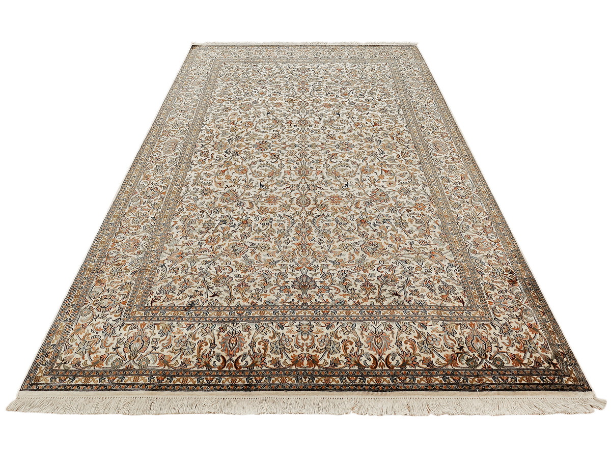 Beige patterned silk rug with central panel, ornate border, and short fringe trim