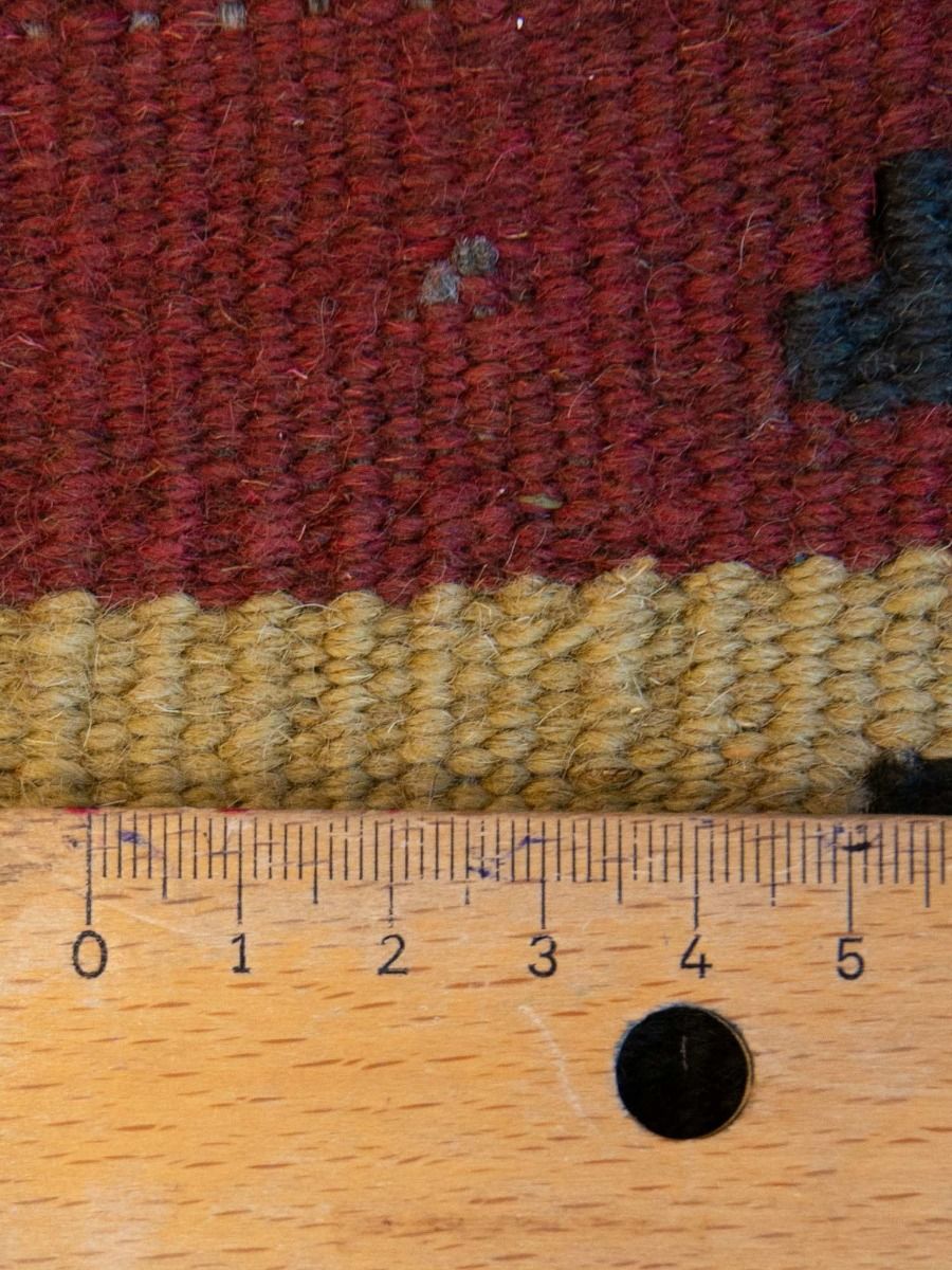 Kilim rug pile texture close-up, maroon and tan blocks; tape measure shows size.