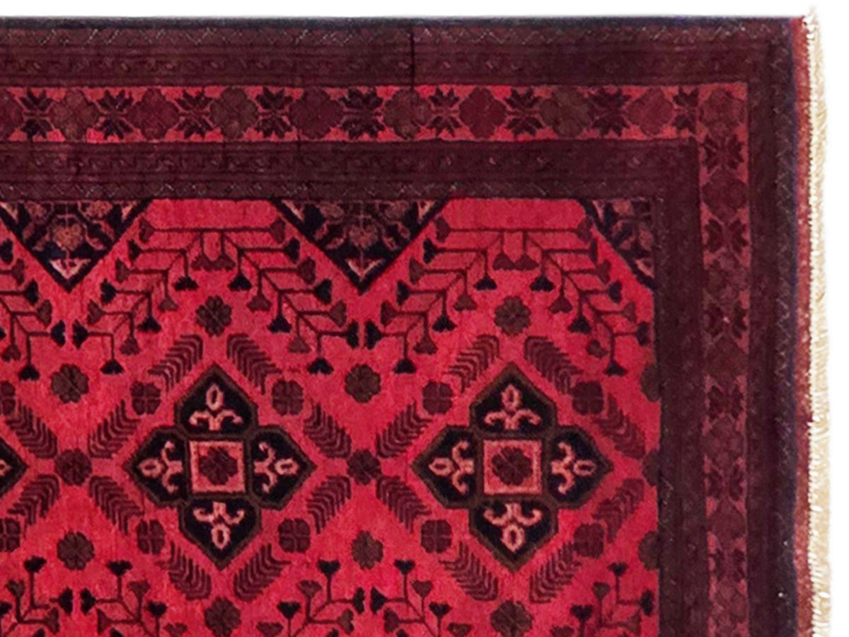 Close-up of red rug with geometric pattern, border details, and fringe edge