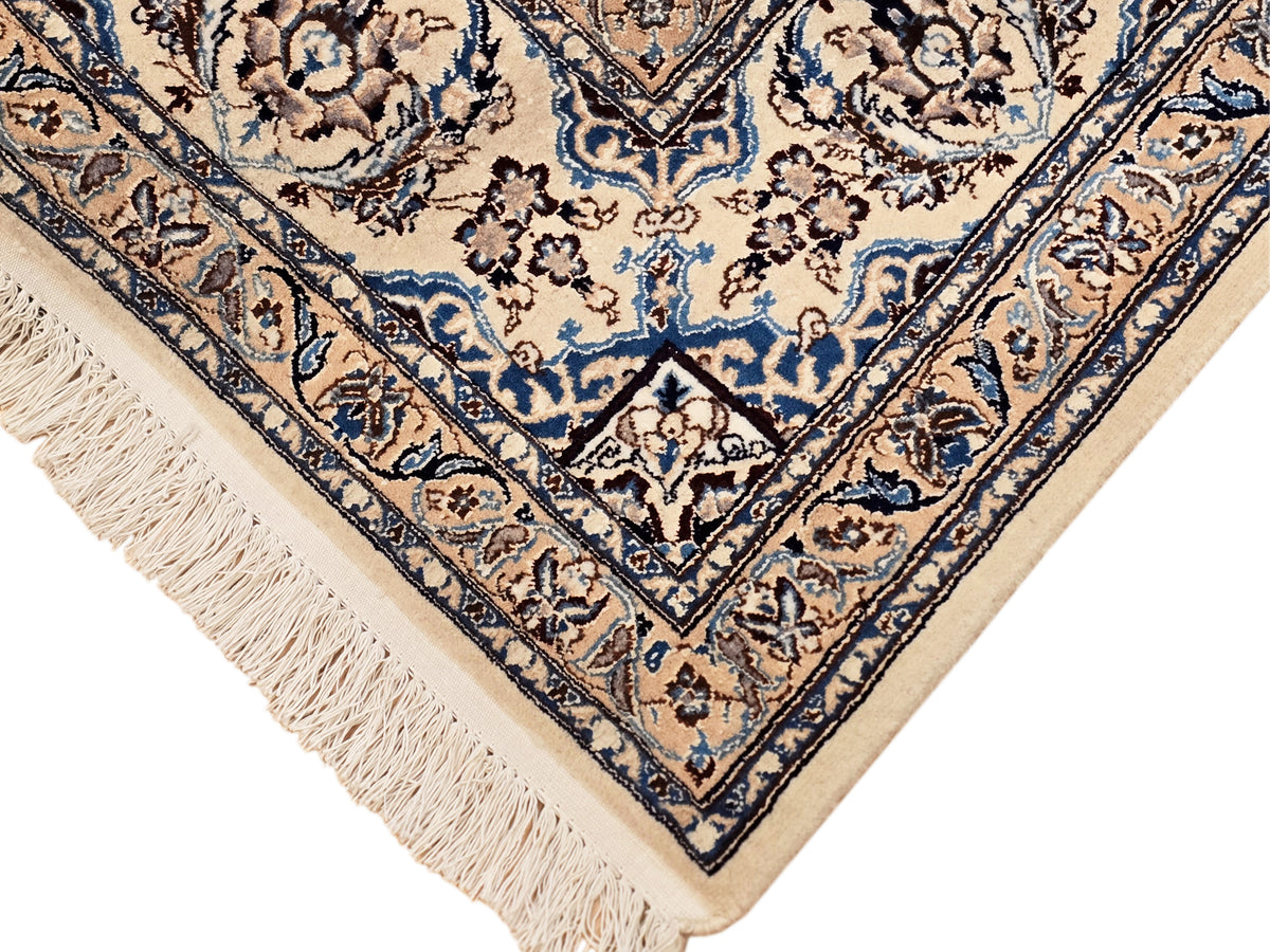 Corner of Nain rug with navy geometric border, cream background, and short fringe