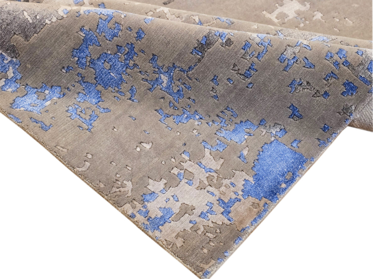 Diagonal view of gray and blue abstract rug with textured distressed pattern