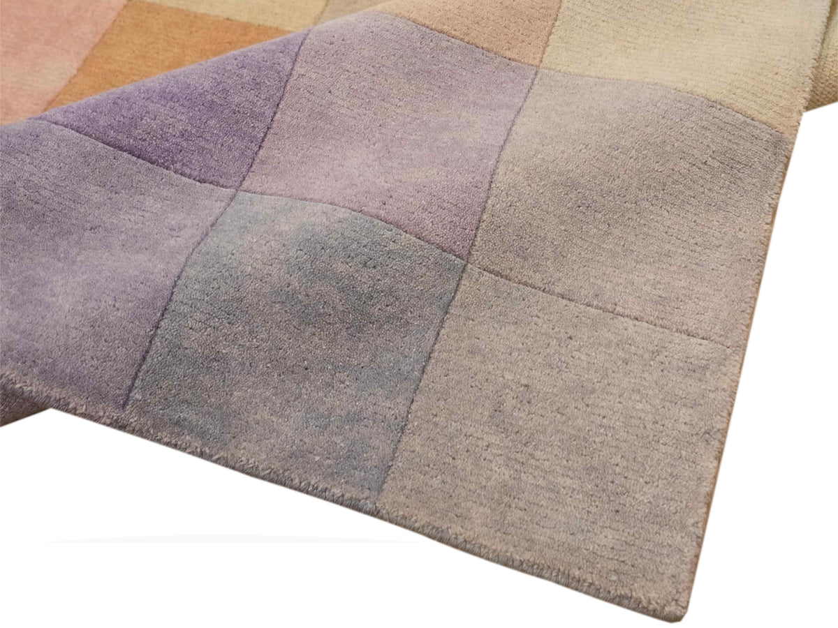 Corner view of square-block rug in lavender, mauve, gray, and beige