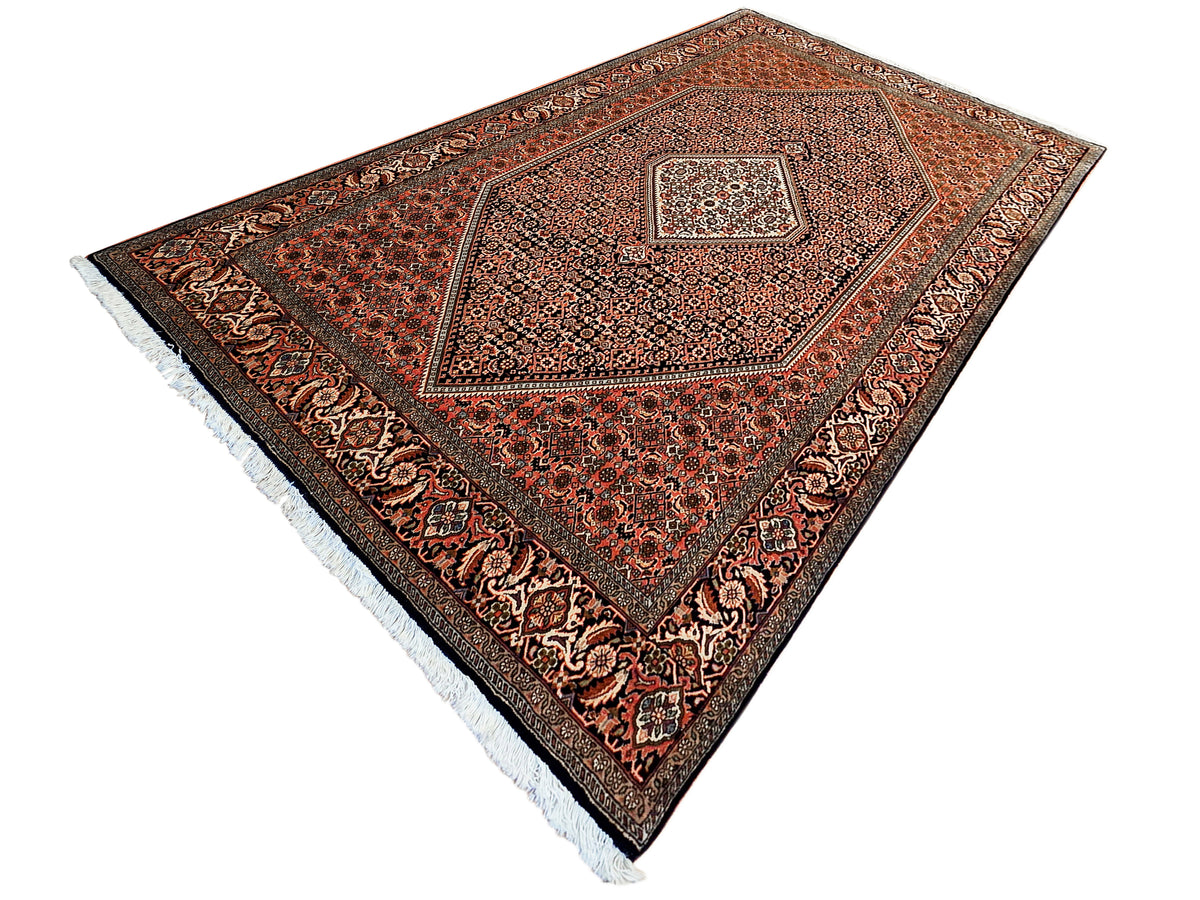 Rust, black and cream patterned area rug with central medallion and light fringe border.