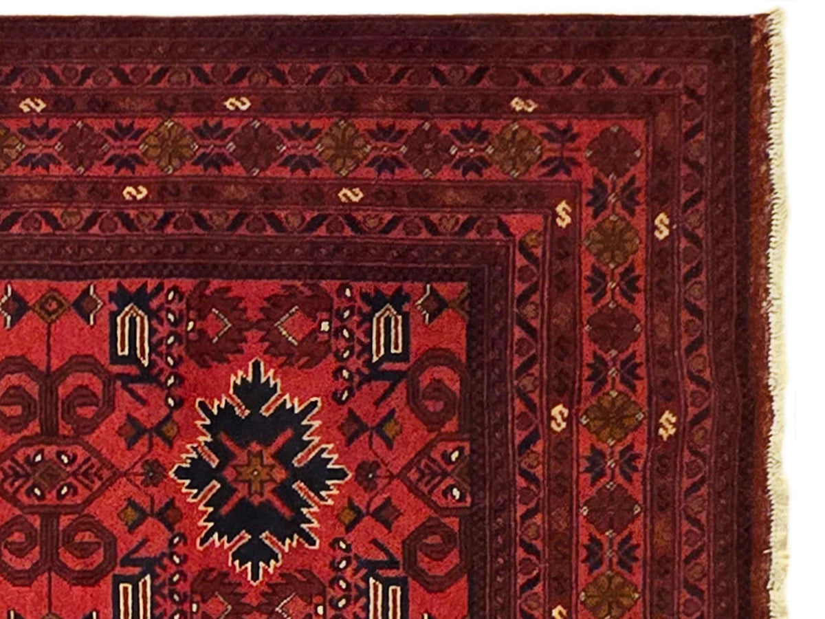 Red patterned area rug with central star-like motif and fringed edge